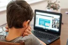 Ein Kind sitzt mit auf den Händen aufgestütztem Kopf vor einem aufgeklappten Laptop