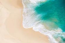 Luftaufnahme einer Welle aus türkisem Wasser, die sich auf einem sandigen Strand bricht